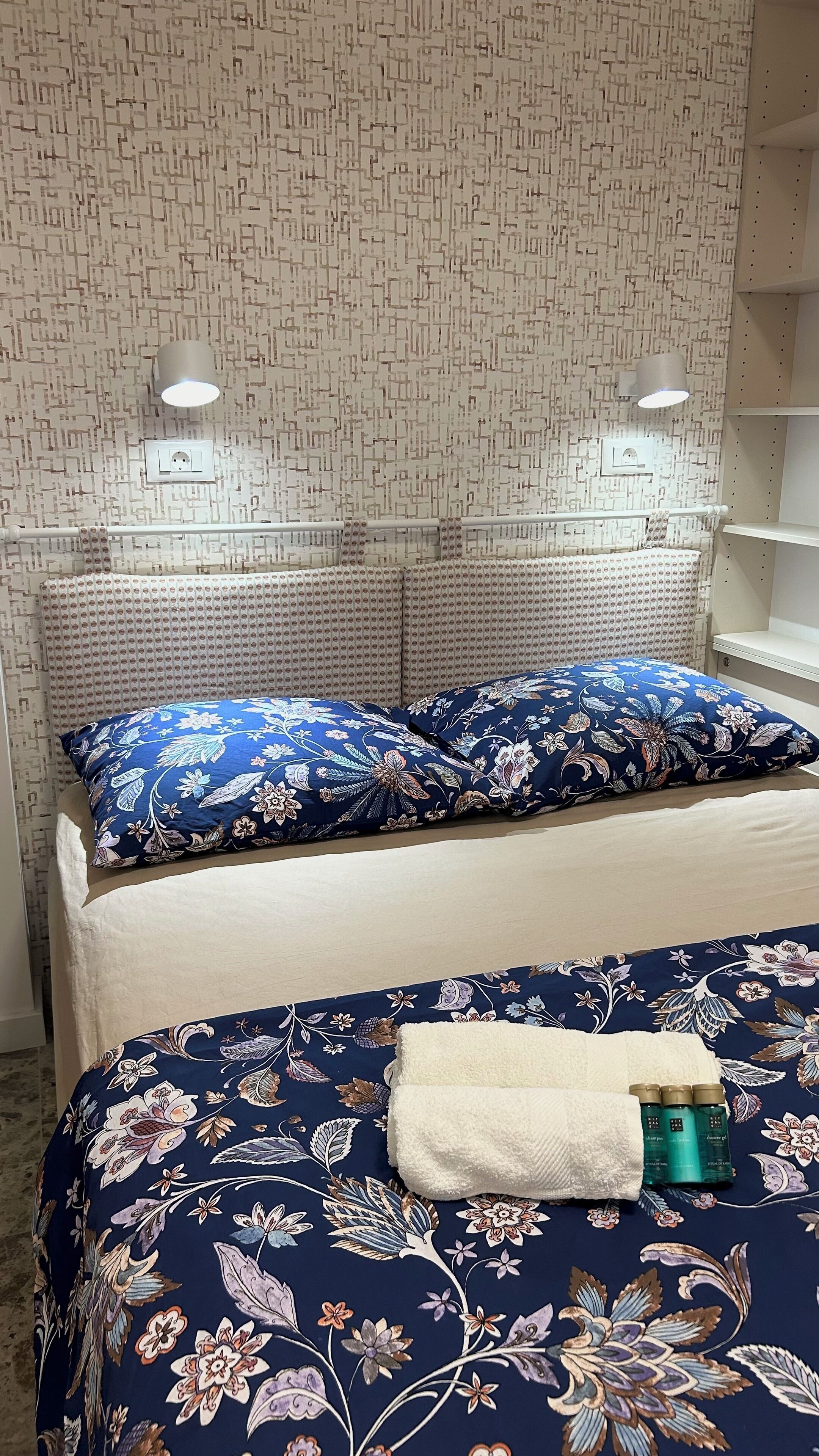 A bed with floral bedding, a blue pillow, and a white towel.