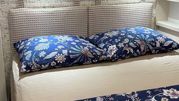 A bed with floral bedding, a blue pillow, and a white towel.