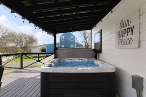 A hot tub on a wooden deck with a pergola overhead. A sign on the wall reads "Our Happy Place."