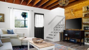 Una sala de estar acogedora con una escalera, un televisor y una estantería.