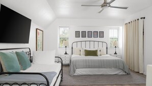 Un dormitorio con cama, mesitas de noche, ventilador de techo y ventana con cortinas.