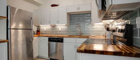 A modern kitchen with stainless steel appliances, white cabinetry, and a tiled backsplash.
