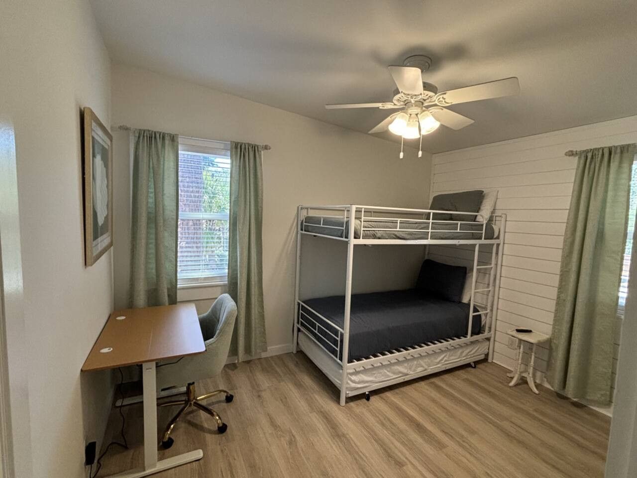 A bunk bed room with a desk, chair, and a ceiling fan.