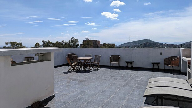 A rooftop terrace with a table and chairs, a small table, and a view of a cityscape and mountains. - Hermoso Departamento Completo, en Tlalnepantla (Tlalnepantla)