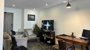A modern living room with a sofa, a TV, a dining table, and a small Christmas tree. - Hermoso Departamento Completo, en Tlalnepantla (Tlalnepantla)