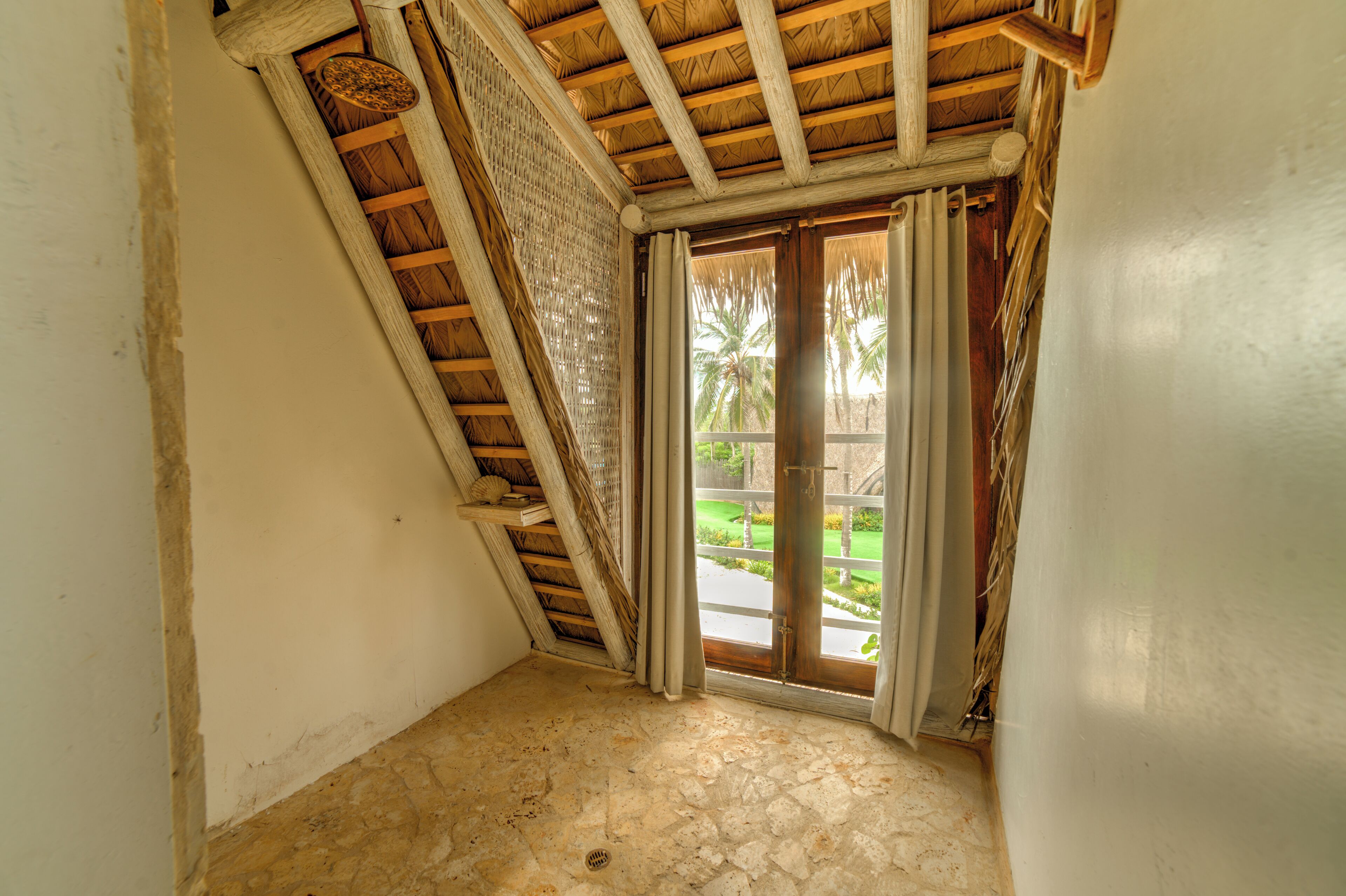 A room with a sloped ceiling, a window with a view of a garden, and a door leading outside.