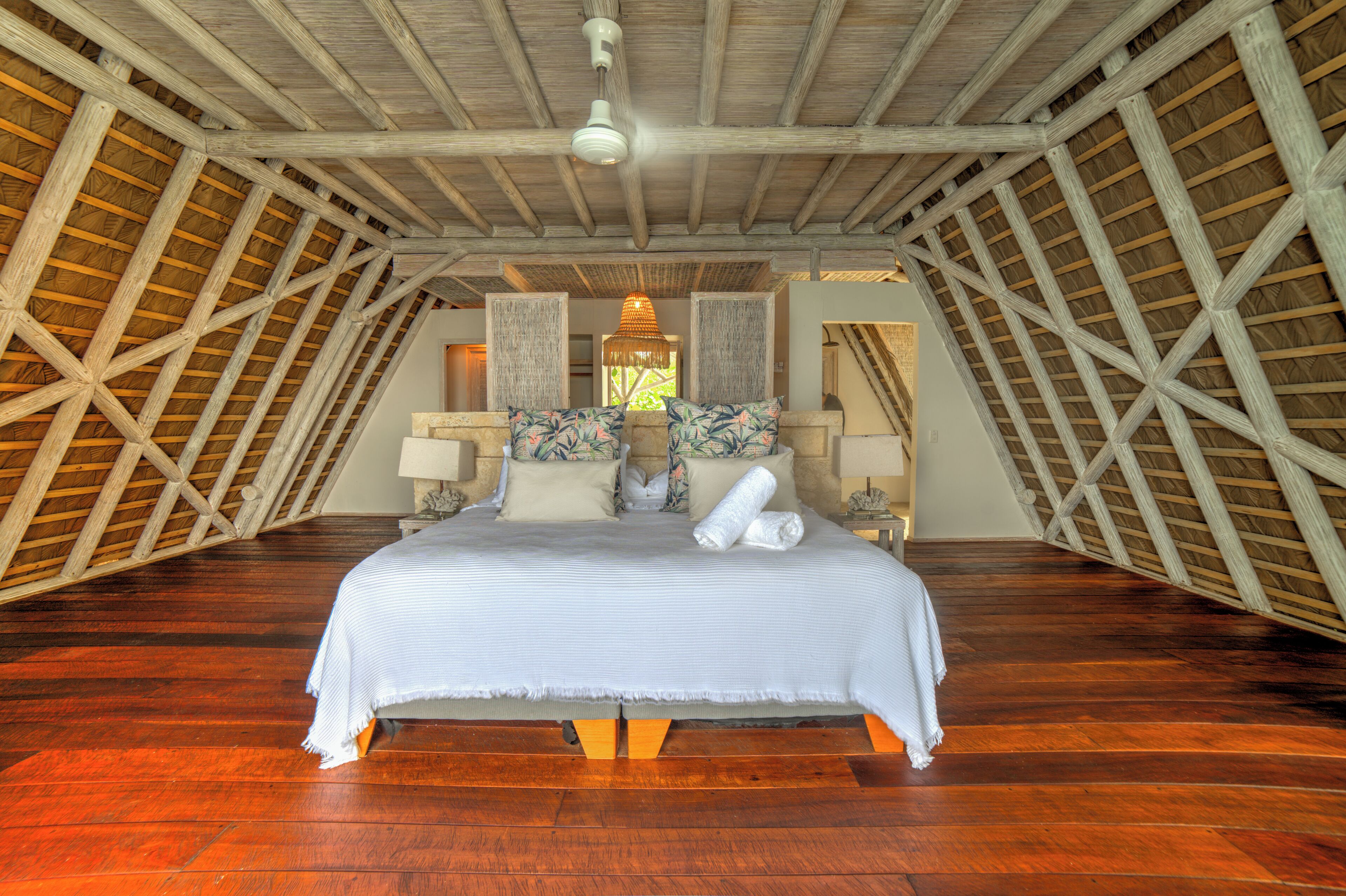 A spacious attic bedroom with a large bed, wooden beams, and a hanging light fixture.
