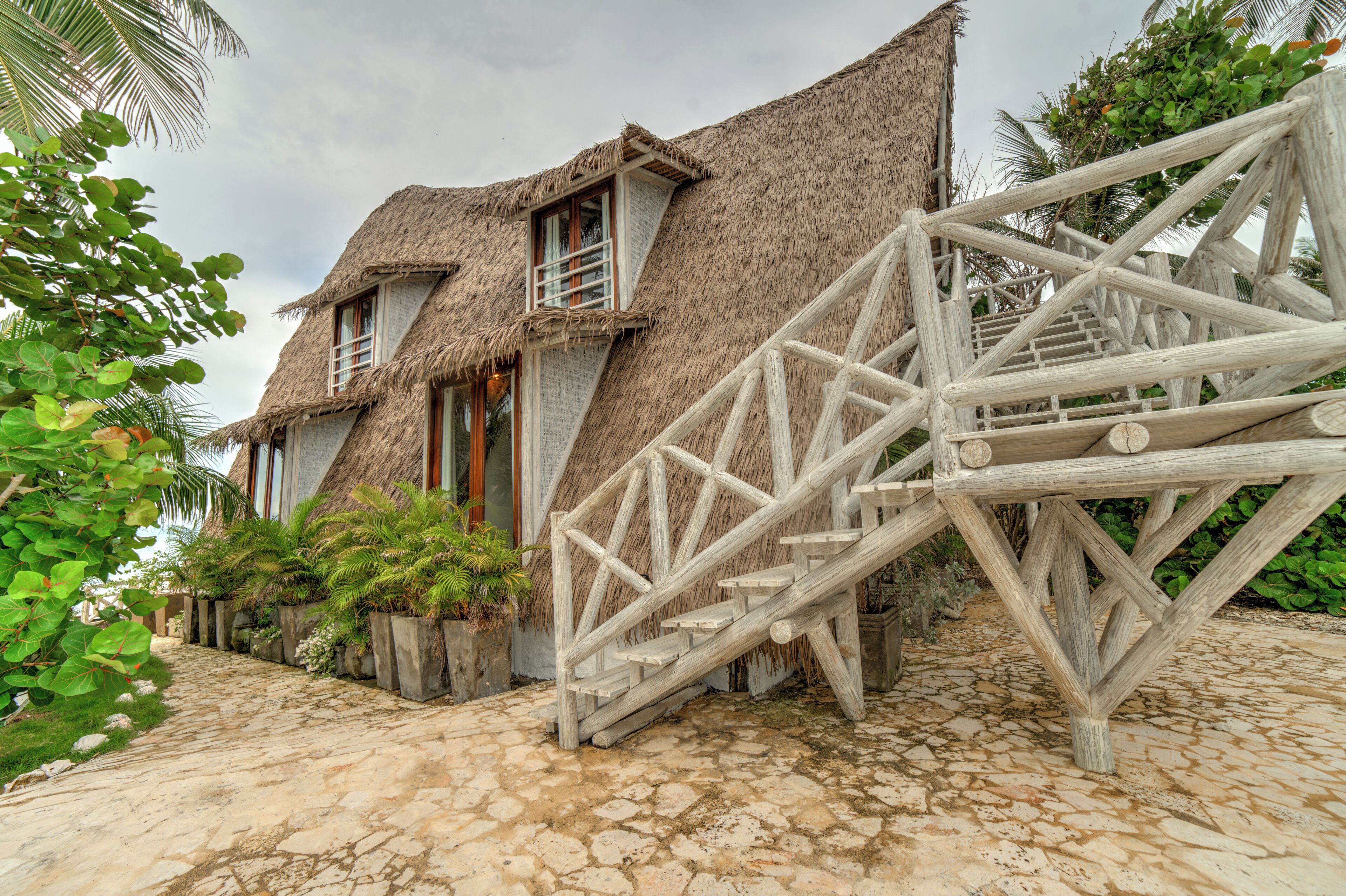 A thatched-roof building with a staircase leading to a wooden deck.