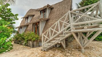 A thatched-roof building with a staircase leading to a wooden deck.