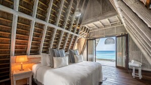A bedroom with a wooden ceiling, a bed with white bedding, a nightstand with a lamp, and a view of the ocean through a door. - Isla Matamba (Rosario Islands)