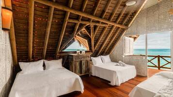 Una habitación con dos camas, suelo de madera, techo de paja y vistas al océano.