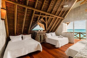 Una habitación con dos camas, suelo de madera, techo de paja y vistas al océano.
