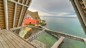 A wooden deck with a netted pool, a thatched-roof building, and a view of the sea. - Isla Matamba (Rosario Islands)
