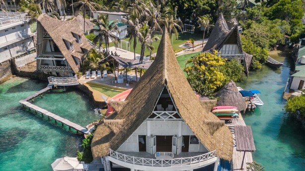 An overwater bungalow with a thatched roof, a wooden deck with lounge chairs, and clear turquoise water. - Isla Matamba (Rosario Islands)