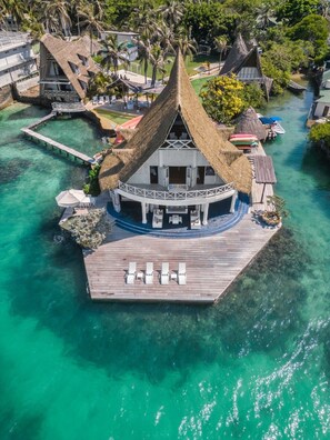 An overwater bungalow with a thatched roof, a wooden deck with lounge chairs, and clear turquoise water. - Isla Matamba (Rosario Islands)