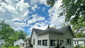 A single-story house with a gabled roof, a front porch with a bench, and a small front yard with a gravel path and potted plants. - 1910 on Route 66 is a Charming historic 2 bedroom 2 bath home, close to downtown (Saint James)