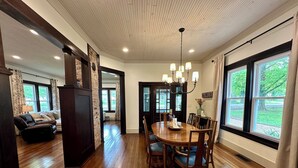 A spacious dining area with a wooden table and chairs, a chandelier, and large windows offering a view of the outdoors. - 1910 on Route 66 is a Charming historic 2 bedroom 2 bath home, close to downtown (Saint James)