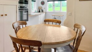 Una cocina con una mesa redonda de madera y sillas, un horno empotrado y una ventana con vistas a la vegetación.