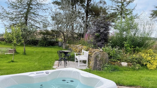 Un jacuzzi en un jardín con césped, una terraza de madera y mobiliario exterior.