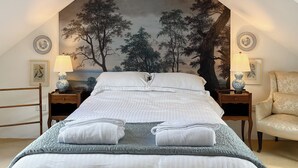 Una cama bien hecha con sábanas blancas y dos toallas dobladas, flanqueada por mesitas de noche con lámparas y marcos con fotografías.