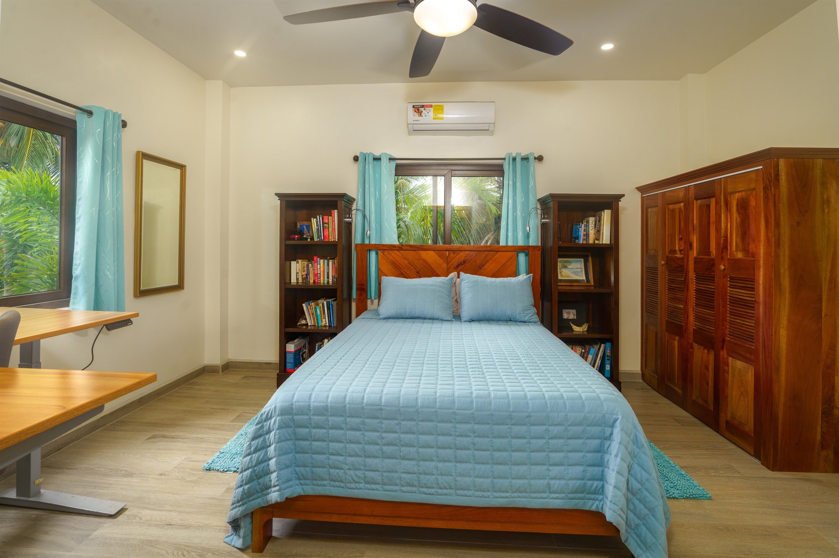 Ein Schlafzimmer mit Bett, Schreibtisch, Bücherregalen, Kleiderschrank und Deckenventilator.