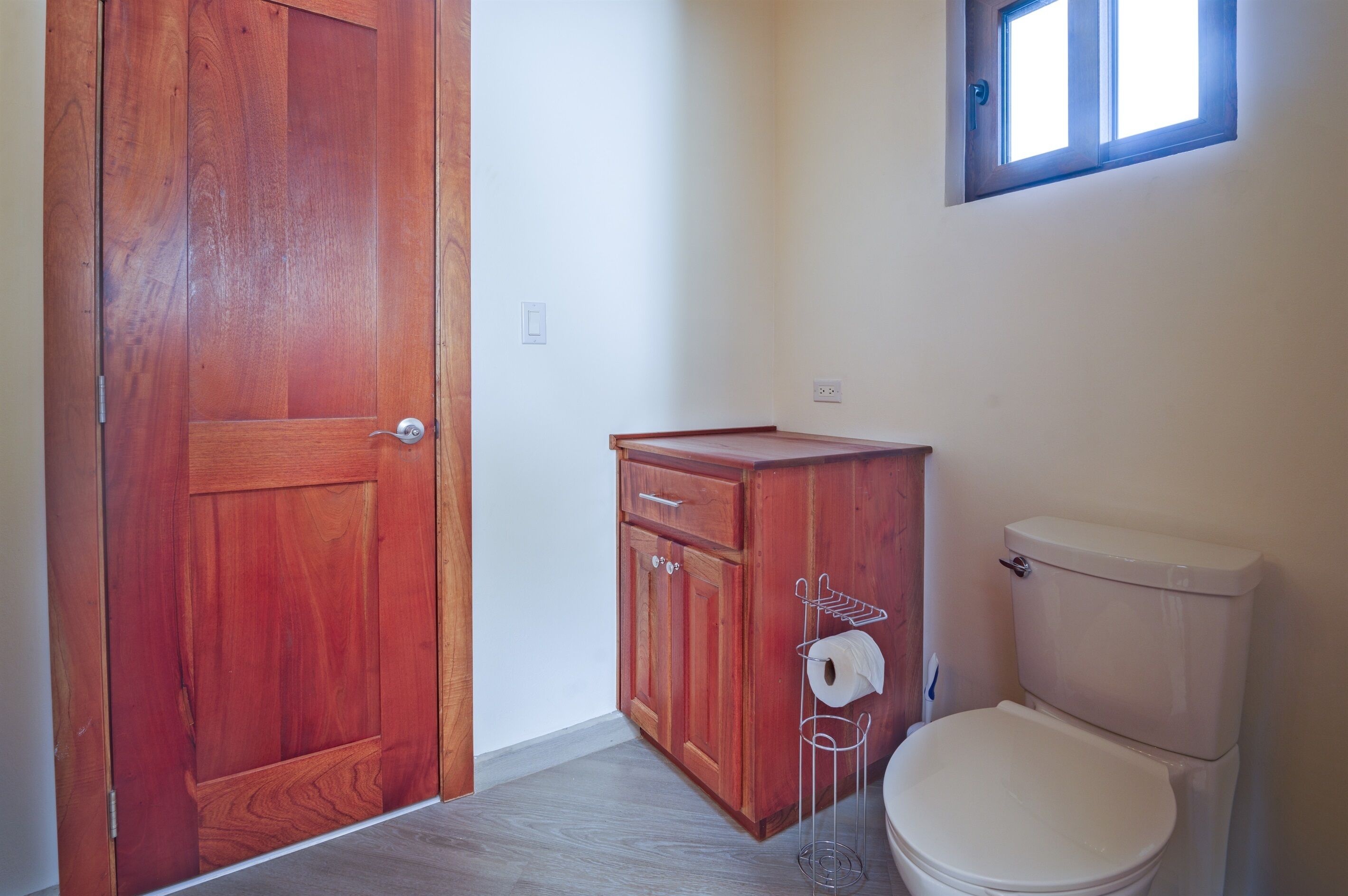 Een badkamer met een houten deur, een houten kastje, een toilet en een raam.