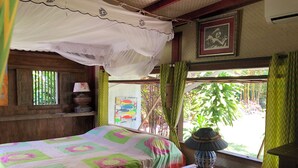 A room with a bed, a nightstand, a window with curtains, a wall-mounted air conditioner, and a framed picture.