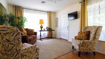 Una sala de estar con sofá, sillón y una mesita de noche con lámpara.