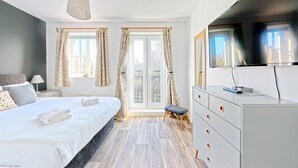 A modern bedroom with a large bed, a grey dresser, a TV, and a window with curtains. - Stunning Coastal Cottage - Sleeping 4 in 2 Bedrooms - Pool and Beach Access Included. (Filey)