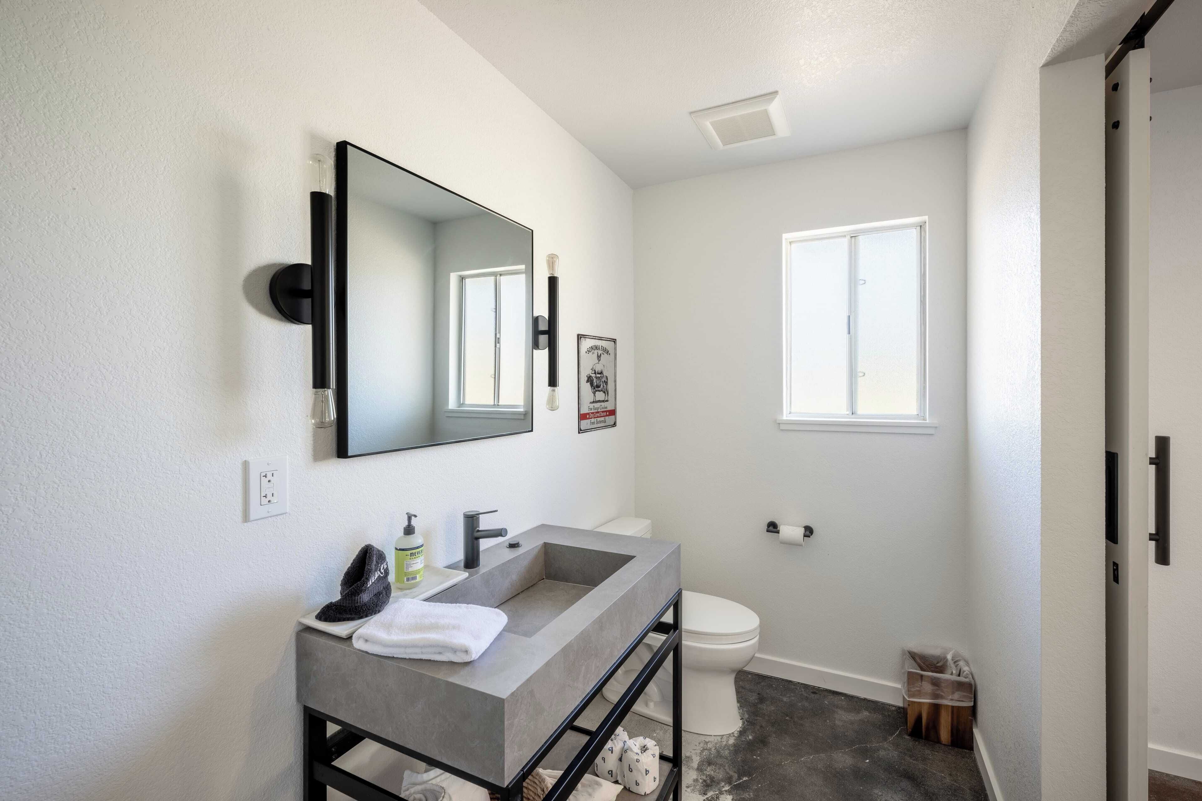 Une salle de bain moderne avec un lavabo gris, un grand miroir et des toilettes blanches.