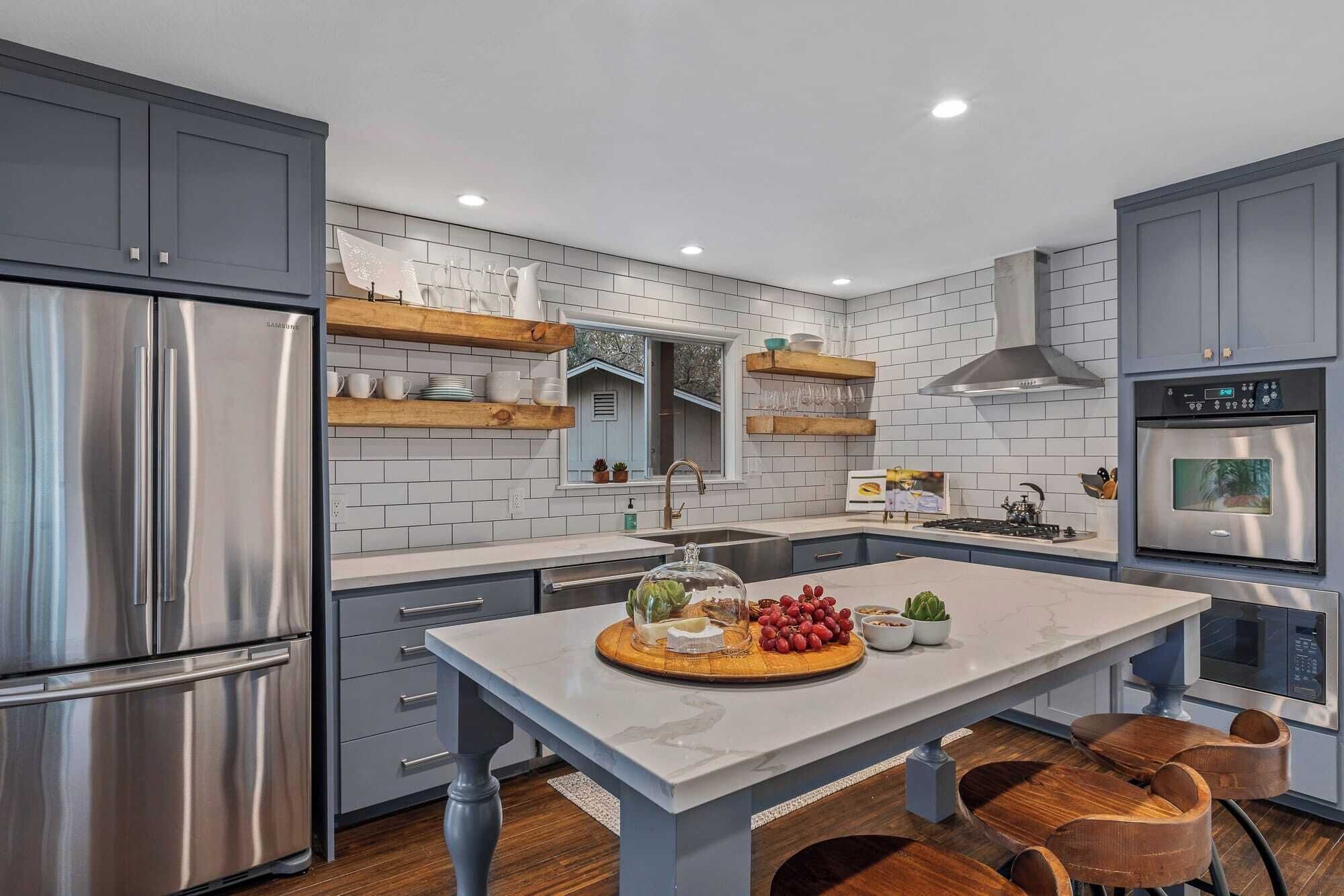 A modern kitchen with grey cabinets, stainless steel appliances, wooden shelves, and a central island with a glass dome.