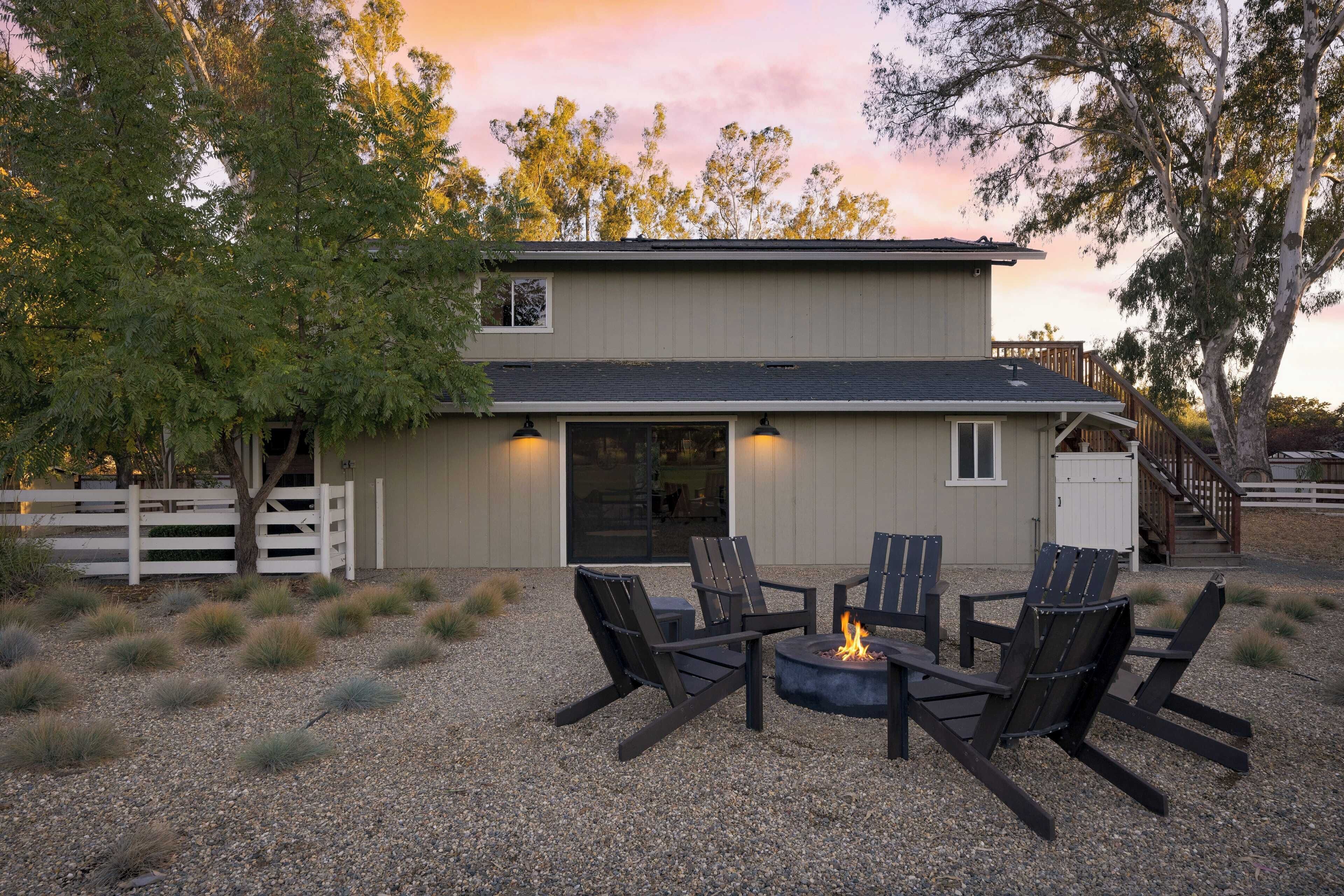 A two-story building with a deck, outdoor seating area with chairs and a fire pit, surrounded by gravel and grass.