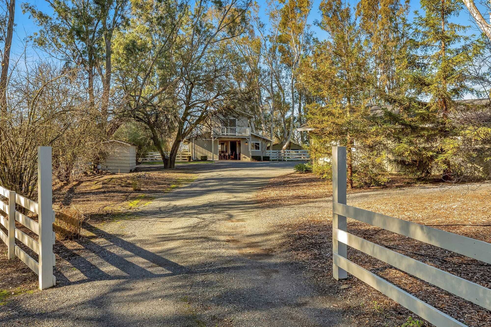 A rural property with a gravel driveway leading to a house with a fenced yard.