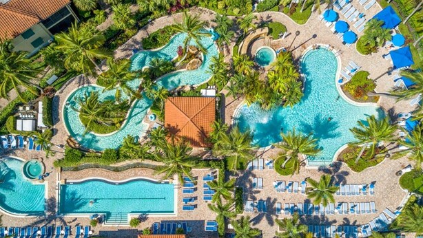An aerial view of a resort with multiple swimming pools, sun loungers, and palm trees. - Oversized 2BR Condo @ Resort near Beach (Naples)