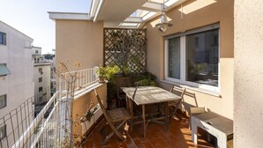 Een balkon met een houten tafel en stoelen, een raam en uitzicht op de stad.