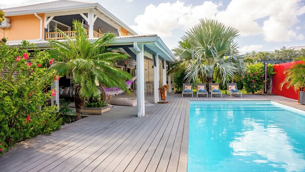 A poolside area with a wooden deck, lounge chairs, and a covered seating area.