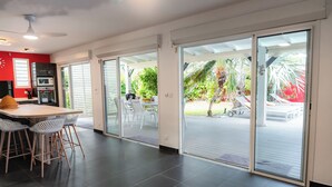 A modern kitchen with a dining area, large sliding glass doors leading to a patio with outdoor furniture and plants.