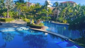 A swimming pool surrounded by palm trees and greenery, with buildings in the background. - Youjia Holiday Apartment Sanya Yalongwan Shenya Feicuigu (Sanya)