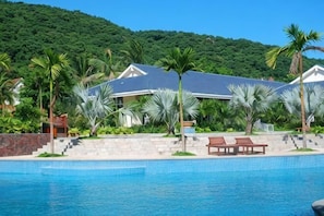 A resort with a swimming pool, palm trees, and a house with a grey roof. - Youjia Holiday Apartment Sanya Yalongwan Shenya Feicuigu (Sanya)