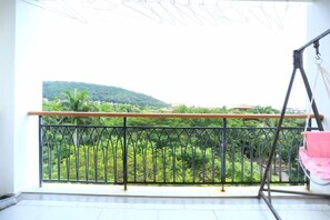 Un balcón con barandilla de metal, una hamaca y vista a un paisaje verde.