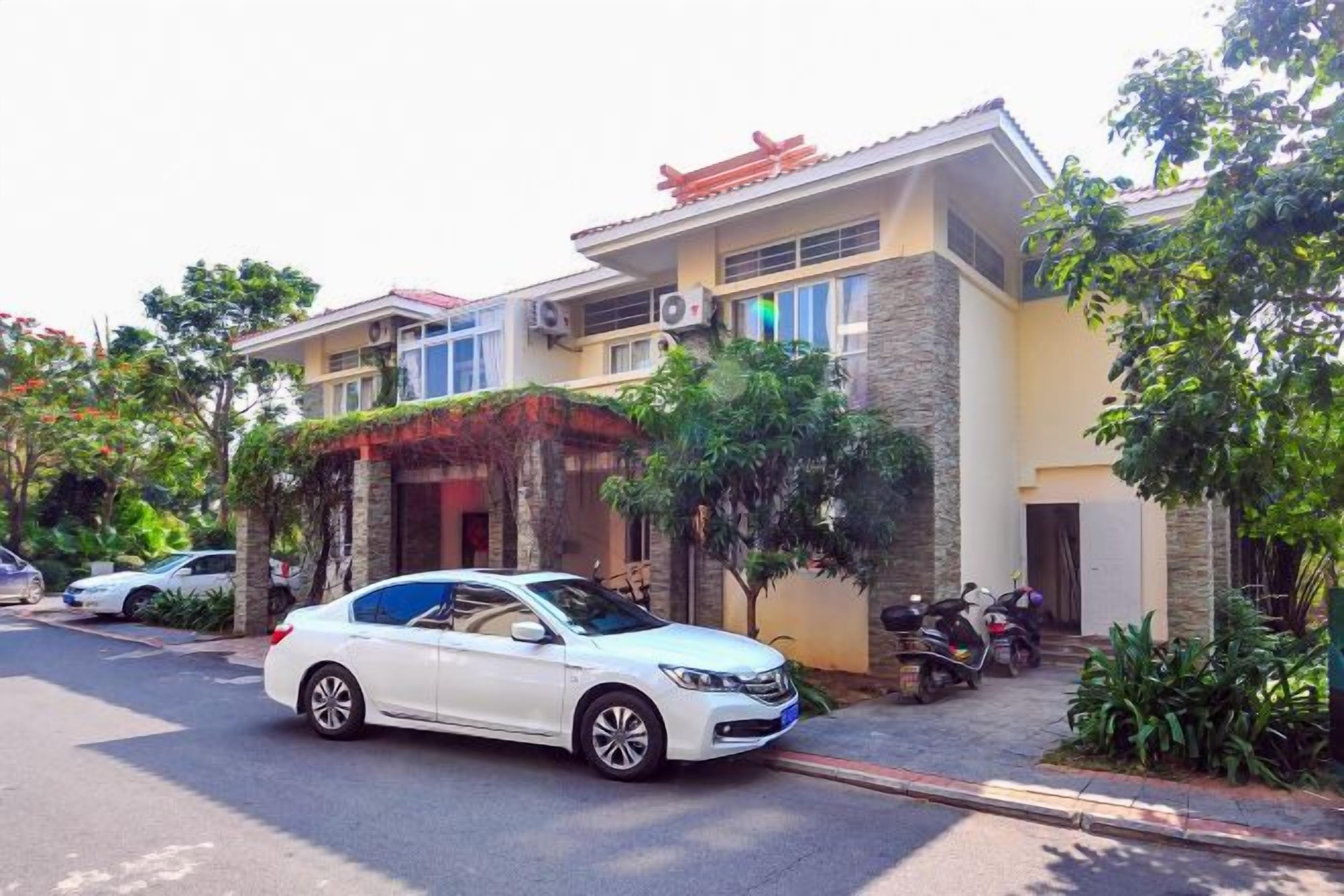 A residential building with a car parked in front, a motorcycle parked outside, and a tree in the foreground.
