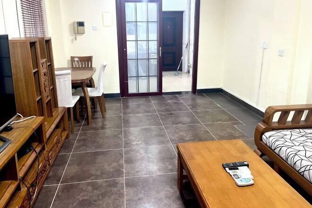 Une pièce comprenant un meuble TV en bois, une table à manger avec des chaises, un canapé et une petite table sur laquelle se trouve une balance.