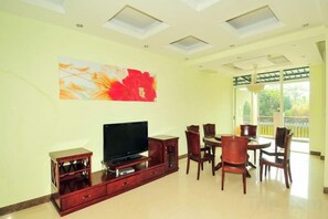 Una sala de estar con televisor de pantalla plana, mueble de madera para entretenimiento, mesa de comedor con sillas y un ventanal con vistas.