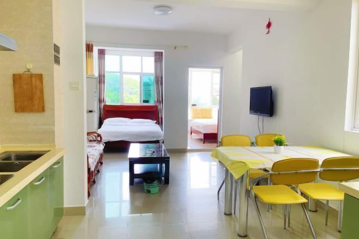 Une chambre d’hôtel comprenant un lit, une télévision, une table à manger avec des chaises, un coin cuisine et une salle de bain visible à travers une porte ouverte.