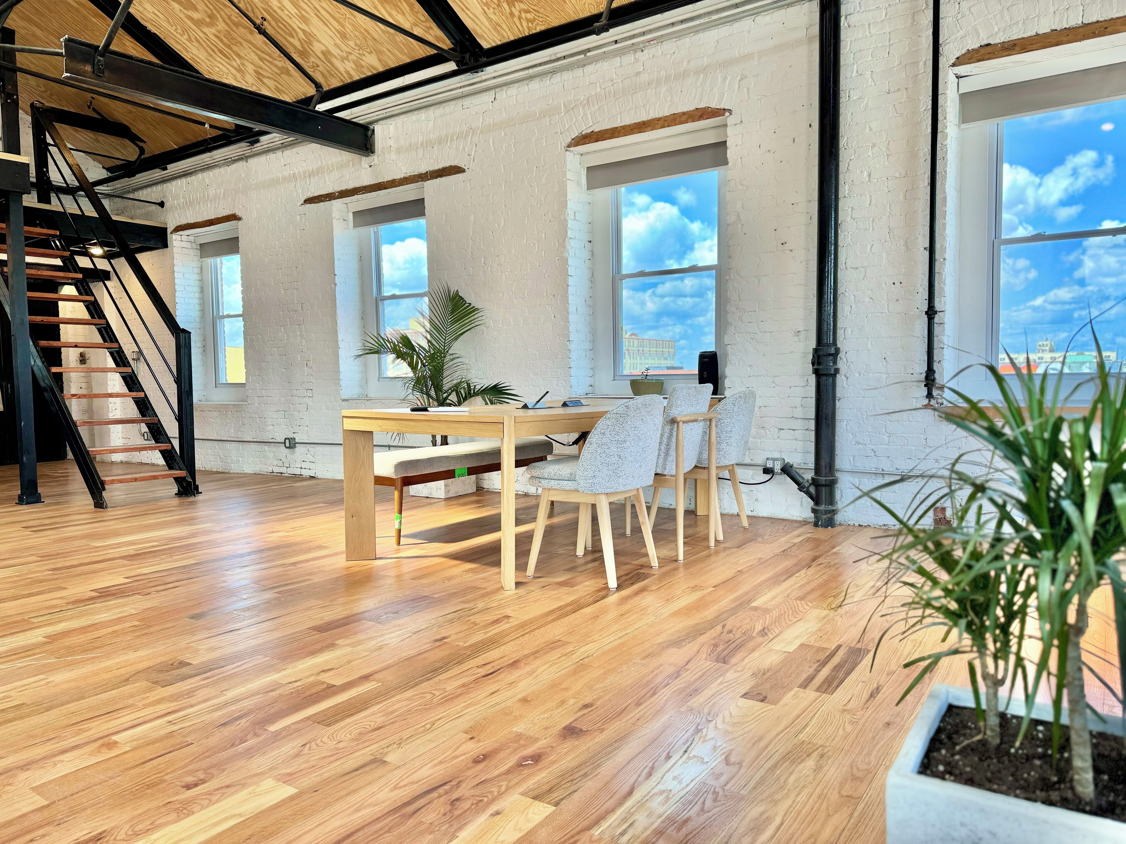 Una habitación amplia con una escalera de madera, una mesa de comedor con sillas y ventanas grandes que ofrecen vistas del cielo.
