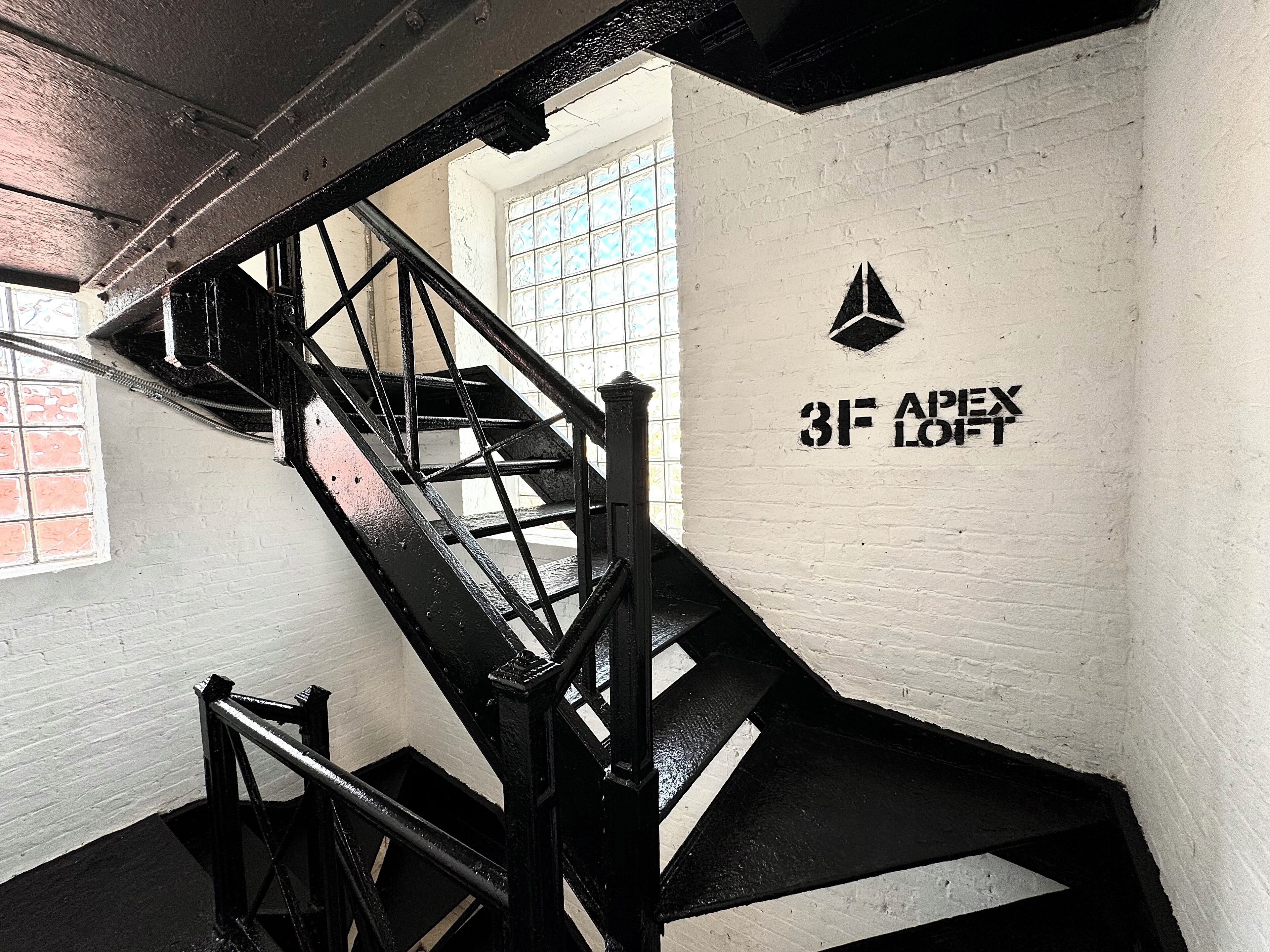 A staircase with black railings and a white wall with a window. There is a sign with the number "3F" and the word "LOFT".