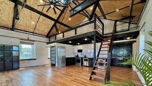 Un loft spacieux avec des poutres apparentes, un parquet disposé en point de Hongrie, un coin cuisine et un escalier central.