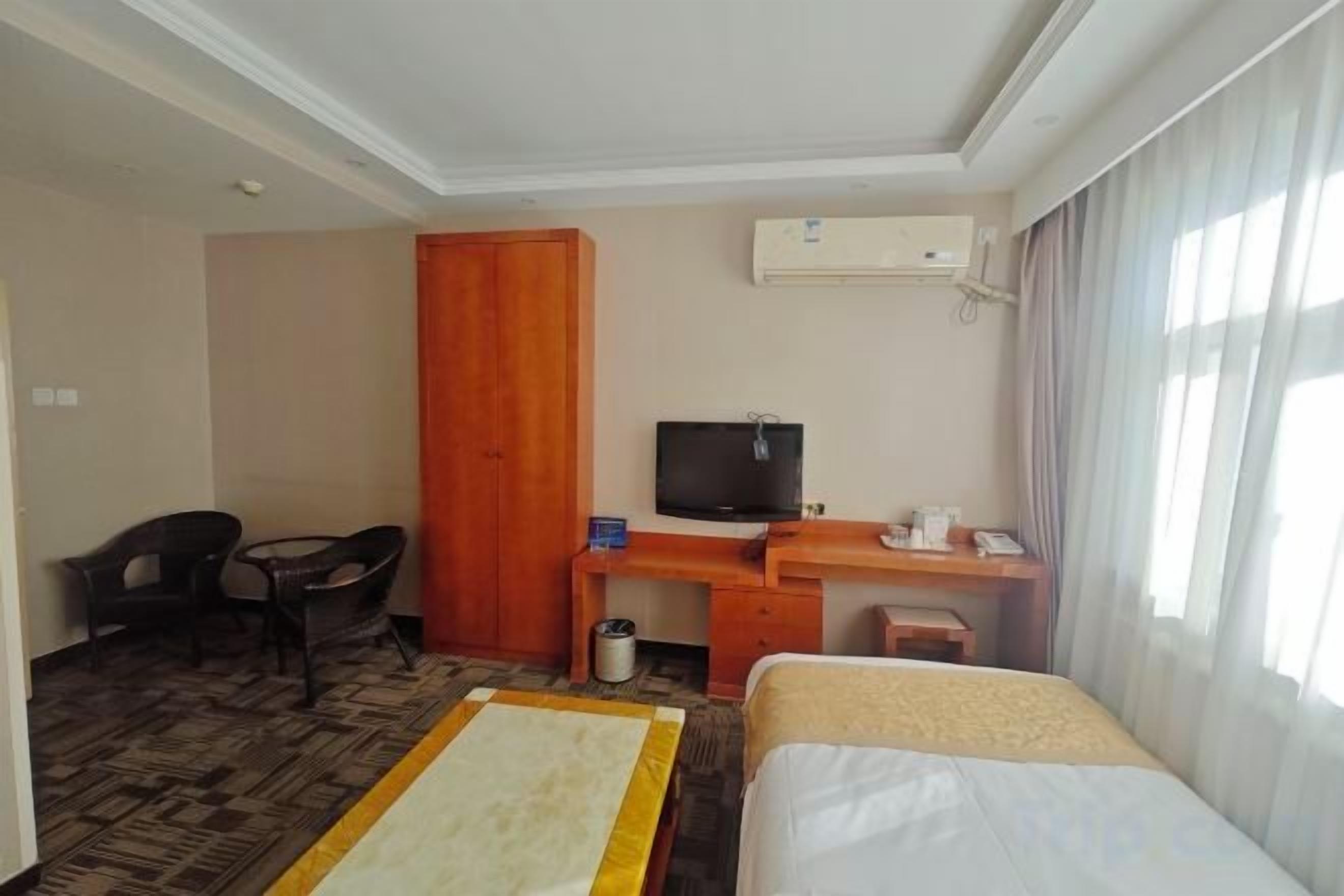 A hotel room with a bed, a desk with a television, a wardrobe, and a chair.