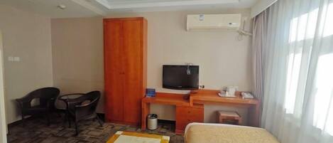 A hotel room with a bed, a desk with a television, a wardrobe, and a chair.