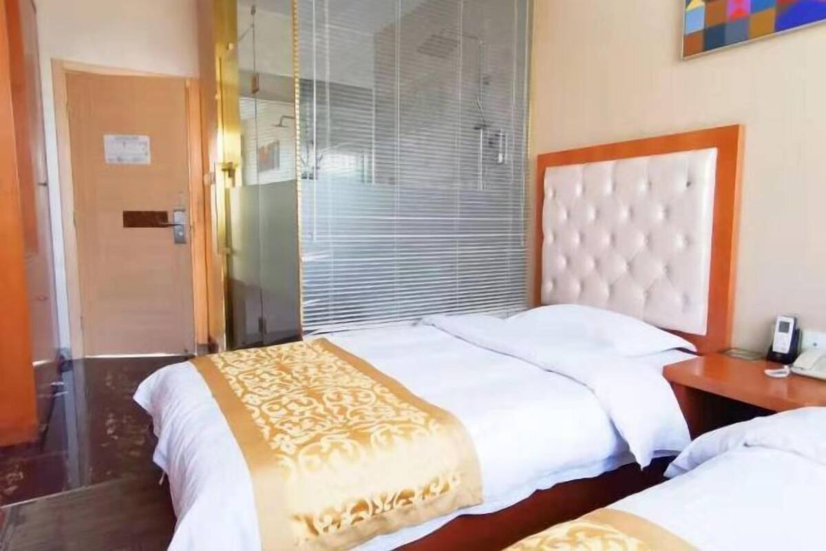 Hotelkamer met twee bedden, een houten hoofdbord, een nachtkastje met een telefoon en een raam met jaloezieën.